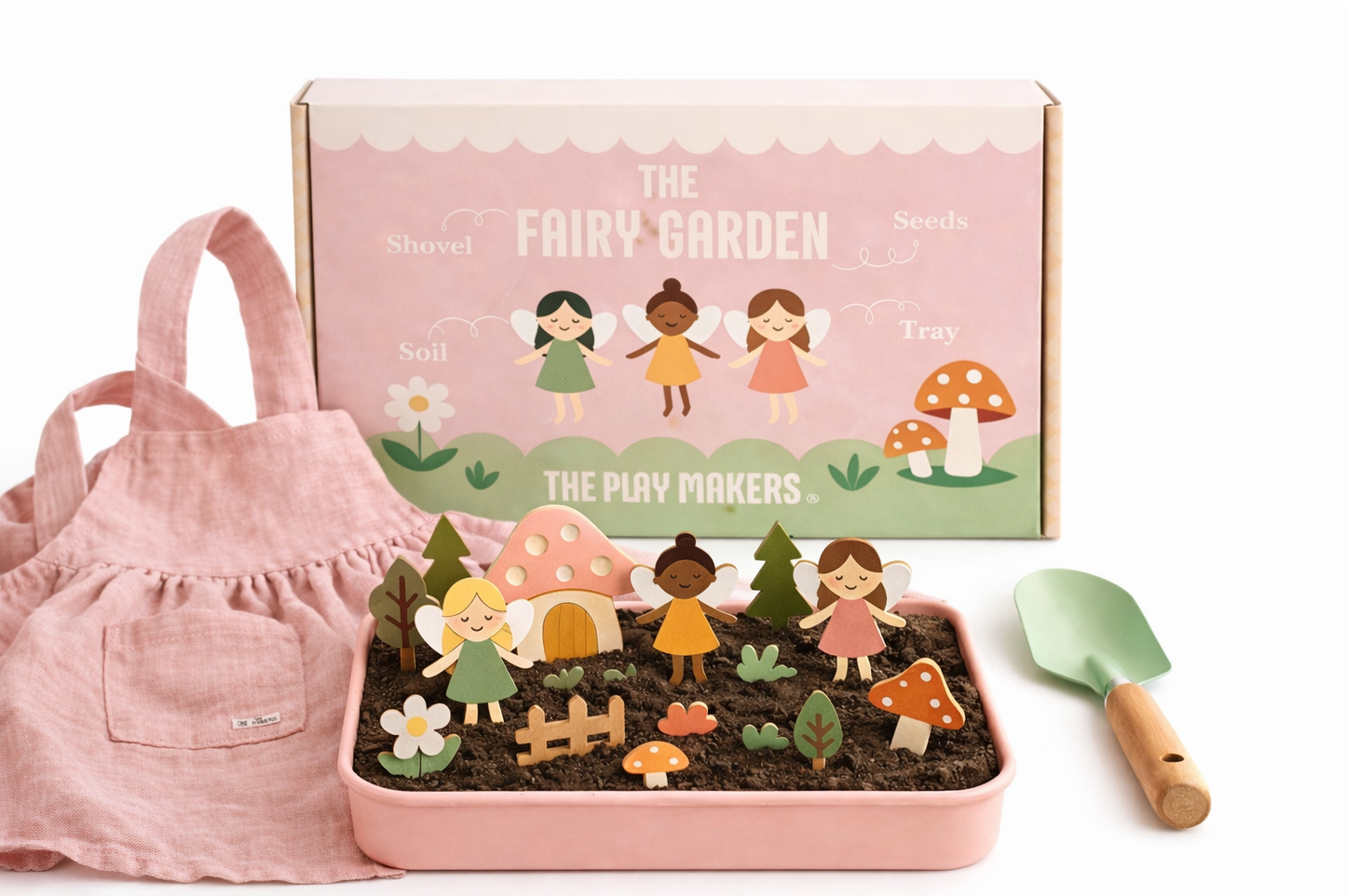Fairy garden set with fairy figures, mushroom, and flower in a pink tray with a pink apron and trowel on a white background.
