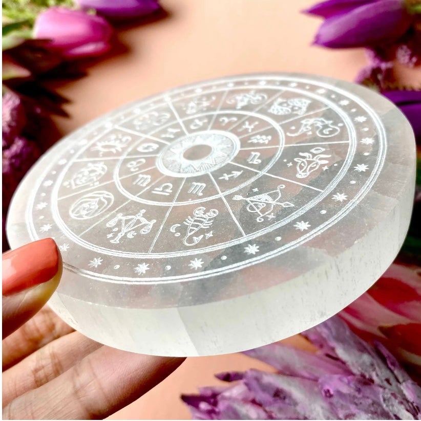 Transparent circular object with astrological symbols held by a hand against a floral background