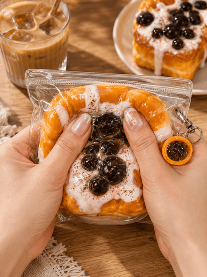 Keychain shaped like a dessert with berries and cream, held by hands on a wooden surface with a glass of iced coffee in the background.