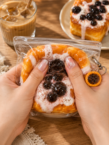 Keychain shaped like a dessert with berries and cream, held by hands on a wooden surface with a glass of iced coffee in the background.