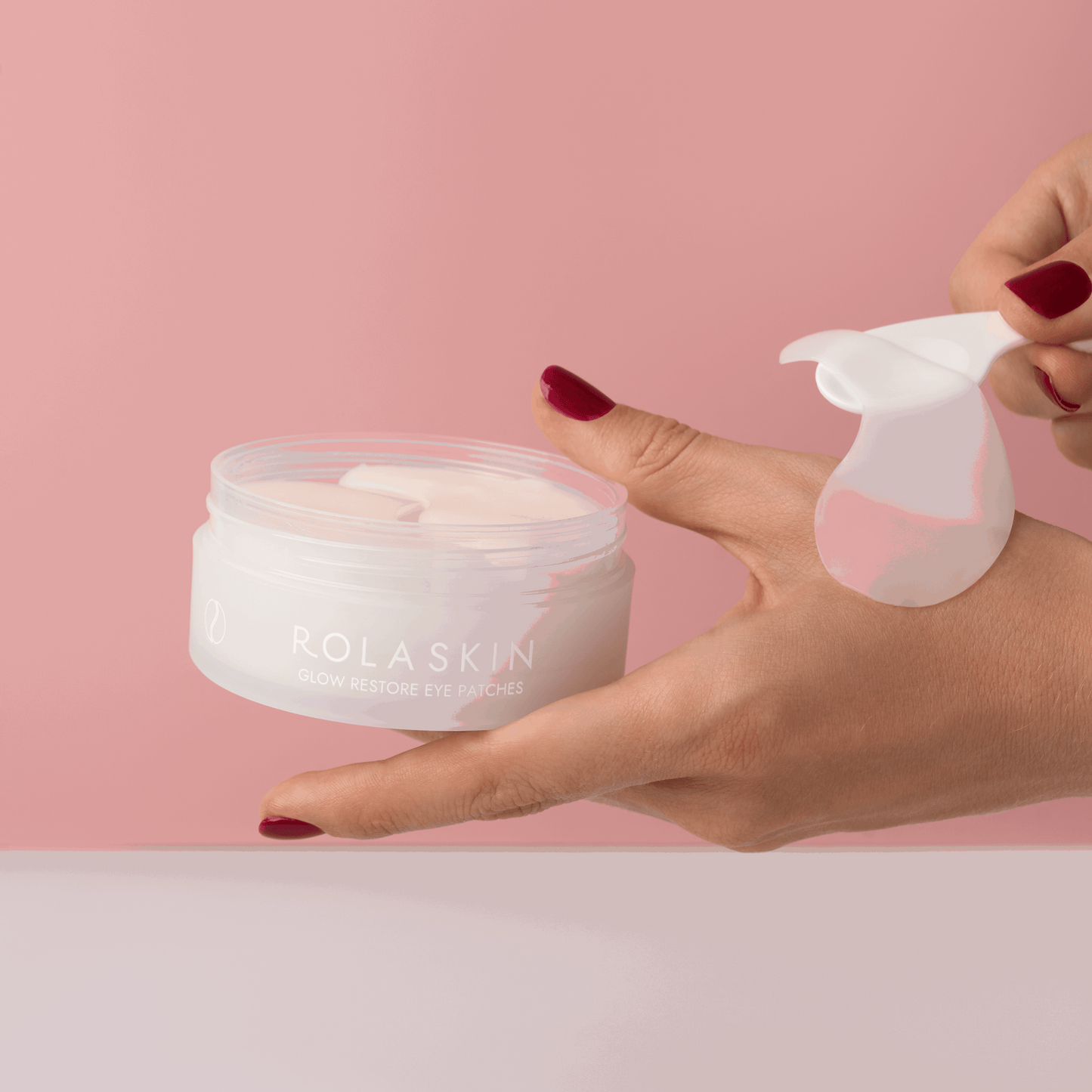 Rolaskin eye patches with a hand holding a container and applying them against a pink background