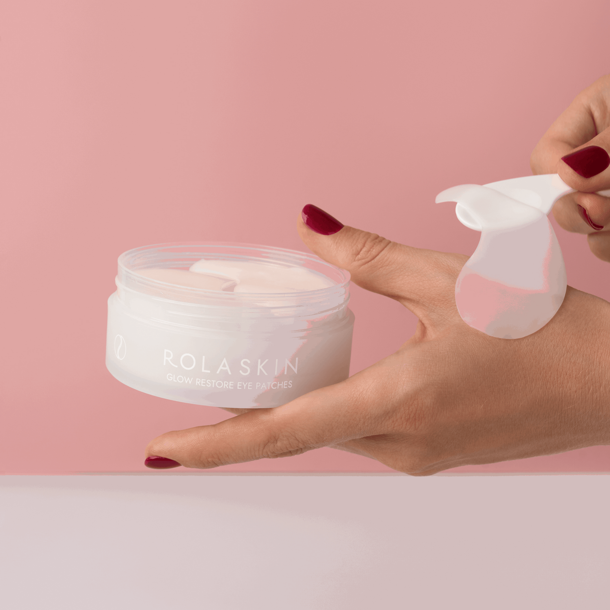 Rolaskin eye patches with a hand holding a container and applying them against a pink background