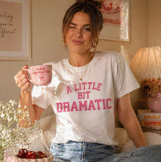 Woman holding a pink mug and wearing a white t-shirt with pink text in a cozy room.