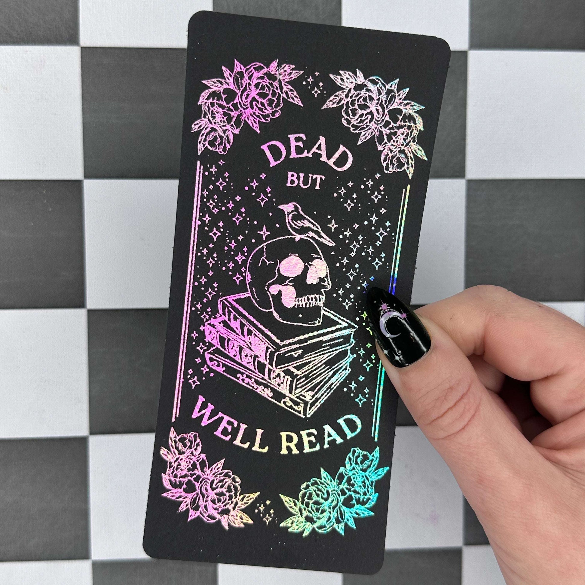 Card with 'Dead but Well Read' design held by a hand on a checkered background