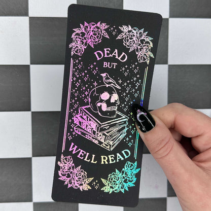 Card with 'Dead but Well Read' design held by a hand on a checkered background