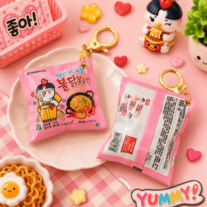 Pink instant noodles package with keychain on a pink checkered tablecloth with decorative items.