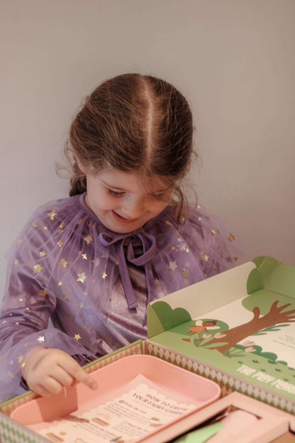 Young girl in a purple dress looking at a book with a tree illustration on a plain background