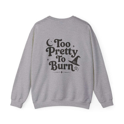 A heather gray crewneck sweatshirt shown from the back, featuring a black graphic print that reads 'Too Pretty To Burn' with a witch hat and stars.