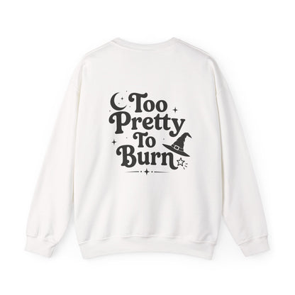 An off-white crewneck sweatshirt shown from the back, featuring a black graphic print that reads 'Too Pretty To Burn' alongside a small witch hat illustration.