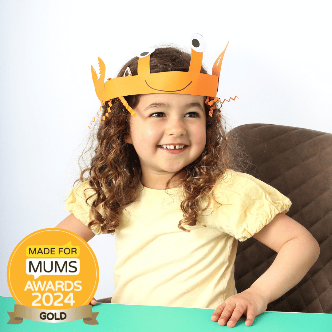 Child wearing a paper crown with a smiley face design, sitting at a table with a 'Made for Mums Awards 2024 Gold' badge.