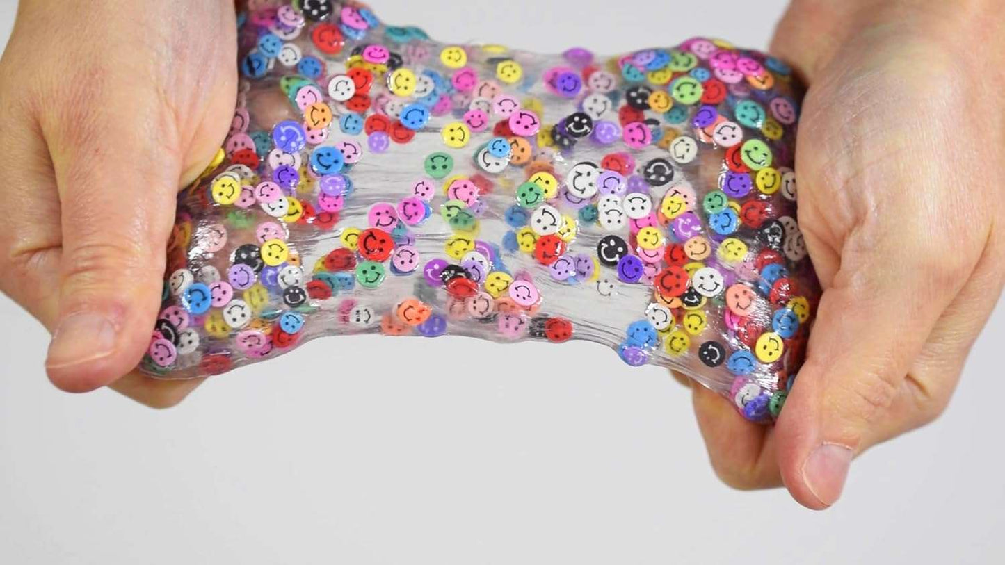 Hands holding a clear slime toy with colorful buttons against a white background