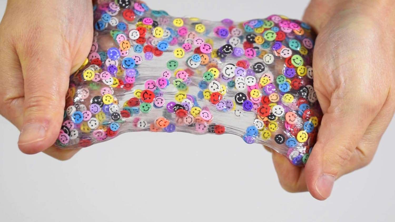 Hands holding a clear slime toy with colorful buttons against a white background