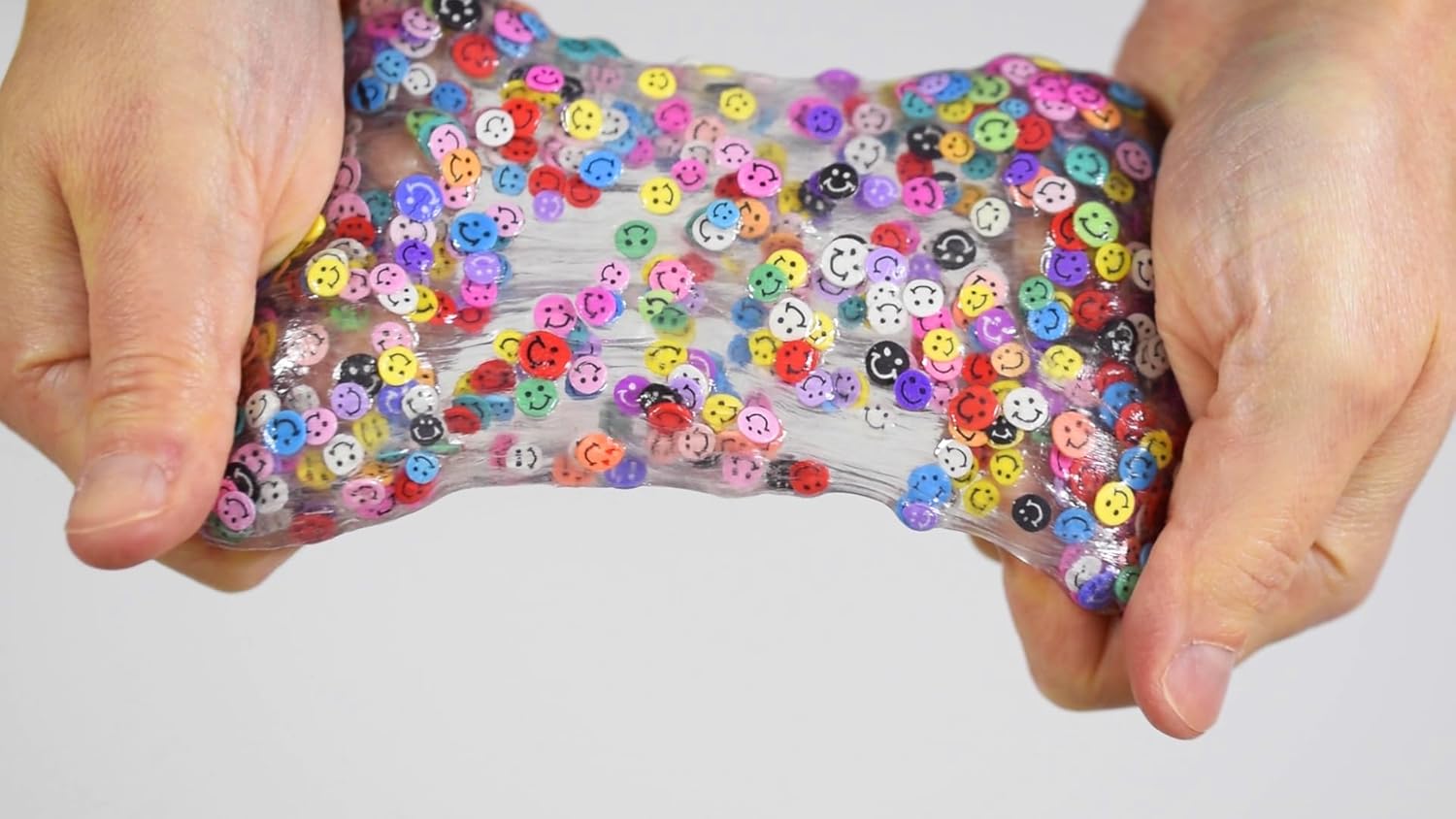 Hands holding a clear slime toy with colorful buttons against a white background