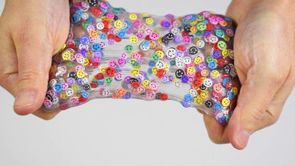 Hands holding a clear slime toy with colorful buttons against a white background