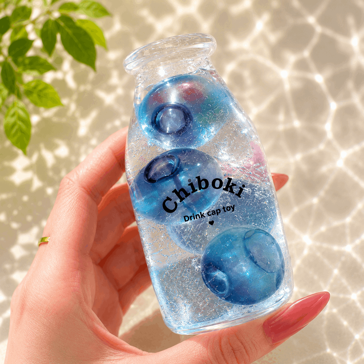 Hand holding a bottle-shaped toy with blue and pink elements and 'Chiboki' branding.