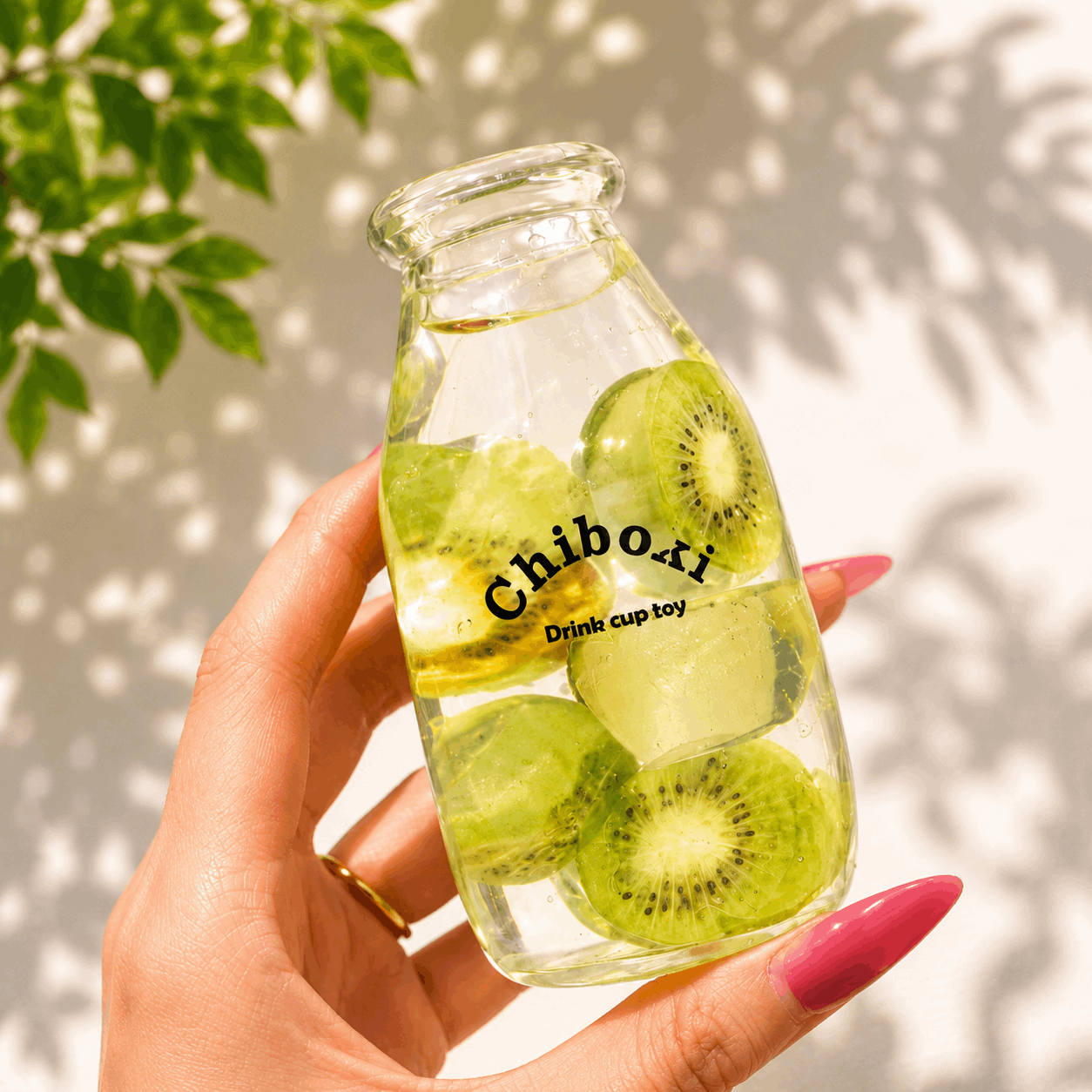 Glass bottle with sliced kiwis labeled 'Chiboki' held by a hand against a light background.