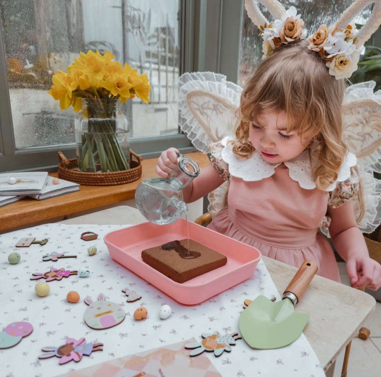 Child in a pink dress with floral headband playing with play food on a table.