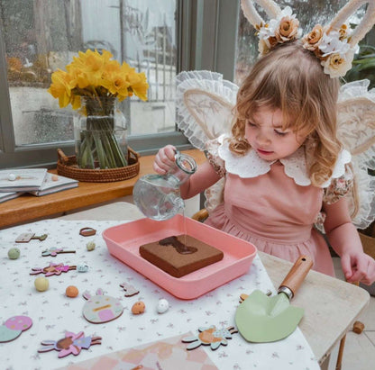 Child in a pink dress with floral headband playing with play food on a table.