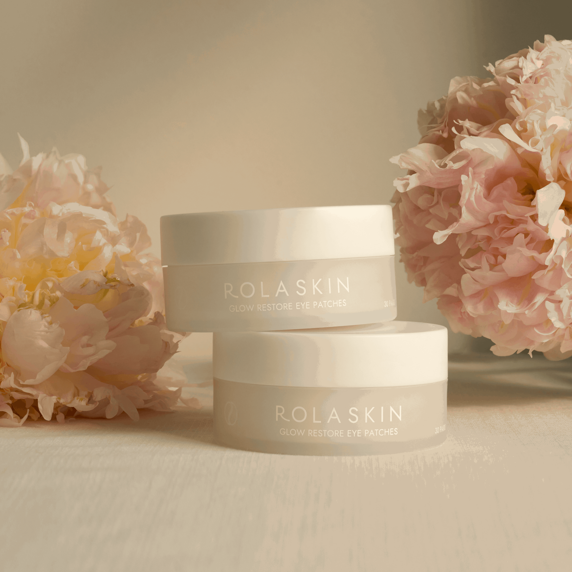 Two Rolaskin eye patches on a beige surface with pink flowers in the background