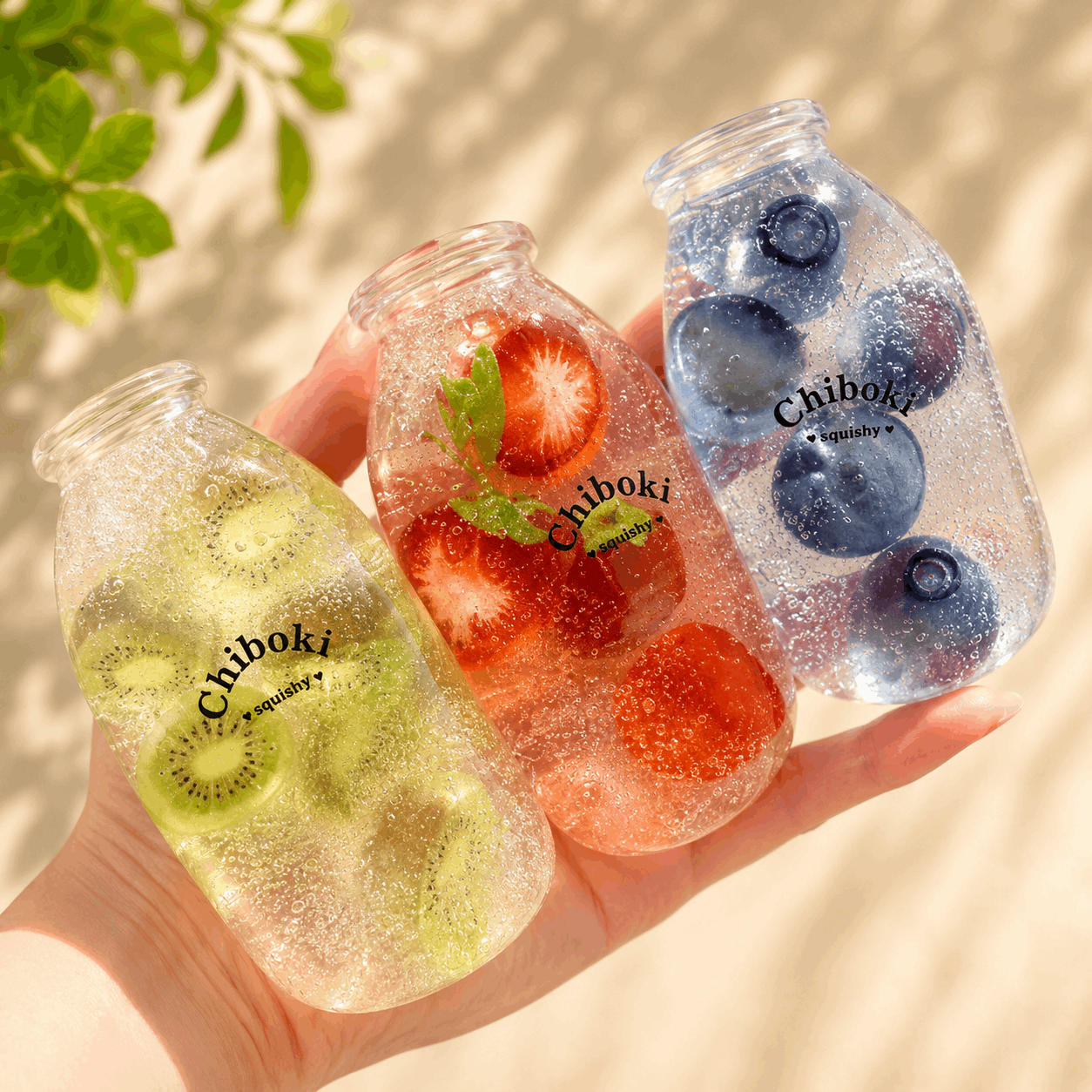 Three Chiboki squishy toys shaped like bottles with fruit inside, held against a light background.