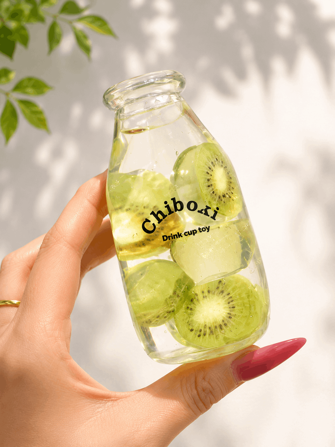 Glass bottle with sliced kiwis and 'Chiboki' branding held by a hand against a light background.