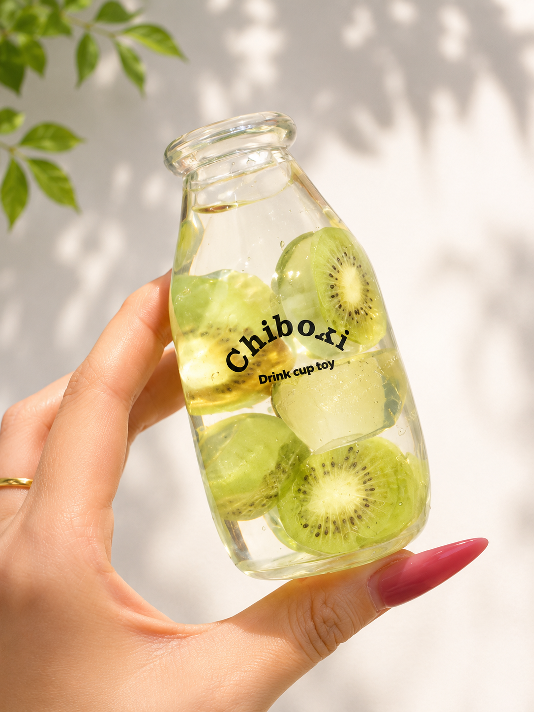 Glass bottle with sliced kiwis and 'Chiboki' branding held by a hand against a light background.