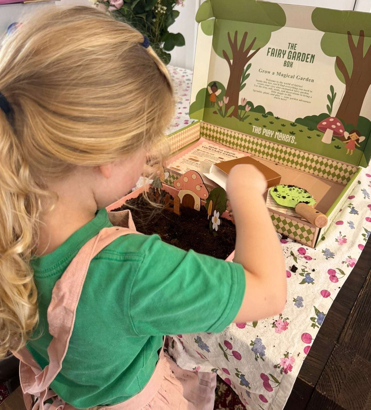 Child playing with a fairy garden kit on a floral tablecloth