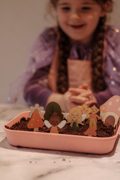 Child with a small garden in a pink container with decorative figures.