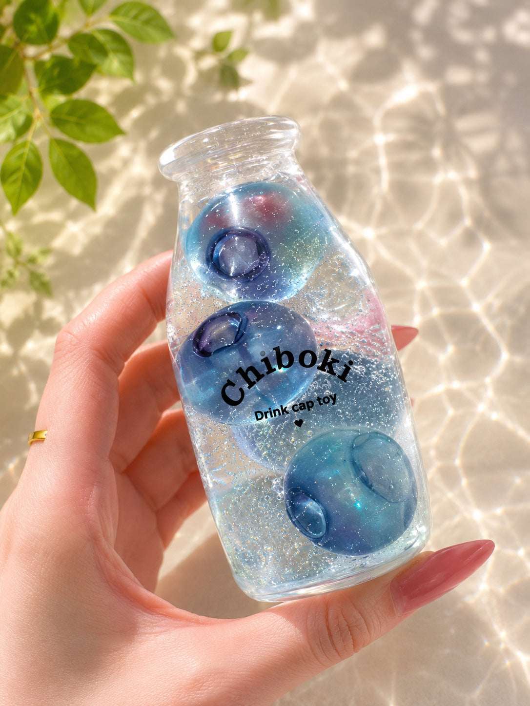 Hand holding a clear bottle with blue and pink gelatinous balls labeled 'Chiboki' against a light background.