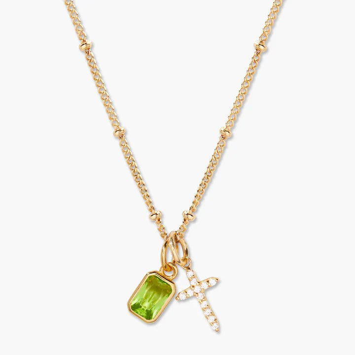 Gold necklace with a green gemstone pendant and cross charm on a white background