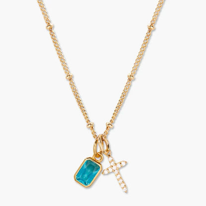 A gold chain necklace featuring a rectangular turquoise gemstone pendant and a small gold cross charm adorned with clear crystals, set against a light gray background.