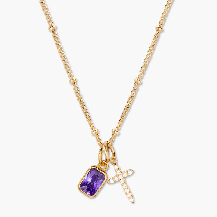 A gold chain necklace featuring a rectangular purple amethyst pendant and a small gold cross charm paved with clear crystals, shown against a light gray background.