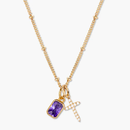 A gold chain necklace featuring a rectangular purple amethyst pendant and a small gold cross charm paved with clear crystals, shown against a light gray background.