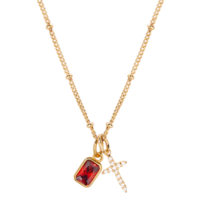 Gold necklace with a red gemstone pendant and cross charm on a white background