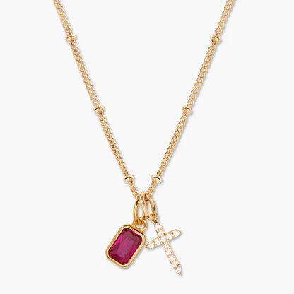 Gold necklace with a red gemstone pendant and cross charm on a white background