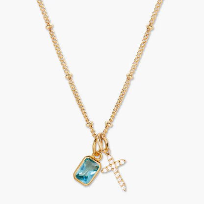 Gold necklace with blue gemstone and cross pendant on a white background
