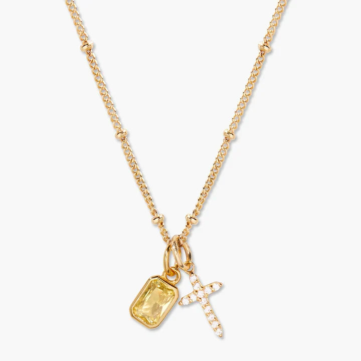 Gold necklace with a yellow gemstone pendant and cross charm on a white background
