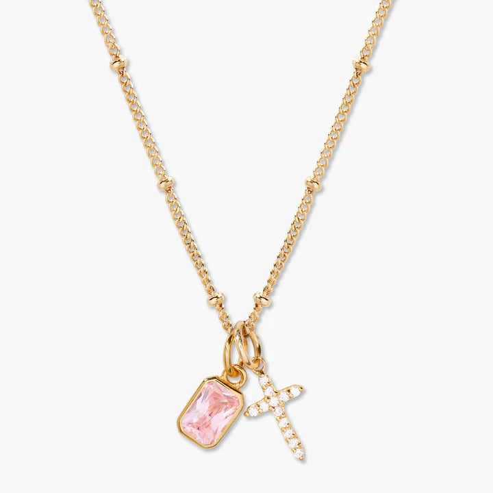 Gold necklace with pink pendant and cross charm on a white background