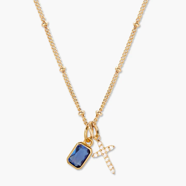 Gold necklace with a blue pendant and cross charm on a white background
