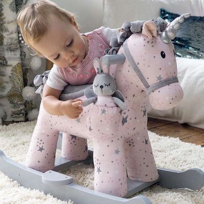 Child playing with a pink rocking unicorn toy on a carpeted floor.