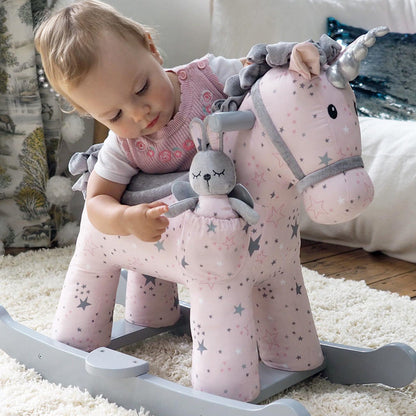 Child playing with a pink rocking unicorn toy on a carpeted floor.