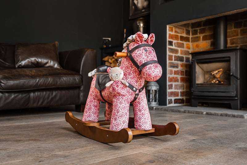 Pink rocking horse toy in a living room with a fireplace.
