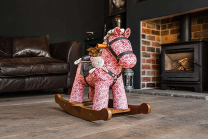 Pink rocking horse toy in a living room with a fireplace.