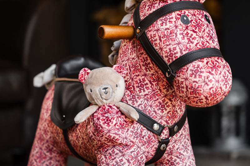 Pink floral-patterned rocking horse with a teddy bear attached, blurred background