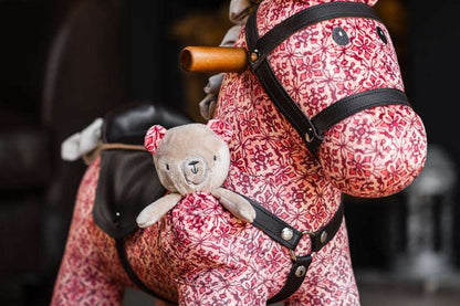 Pink floral-patterned rocking horse with a teddy bear attached, blurred background