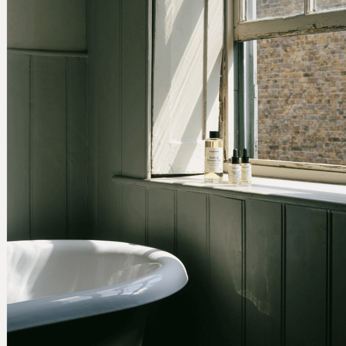 Bathroom with a window sill featuring skincare products and a white bathtub.