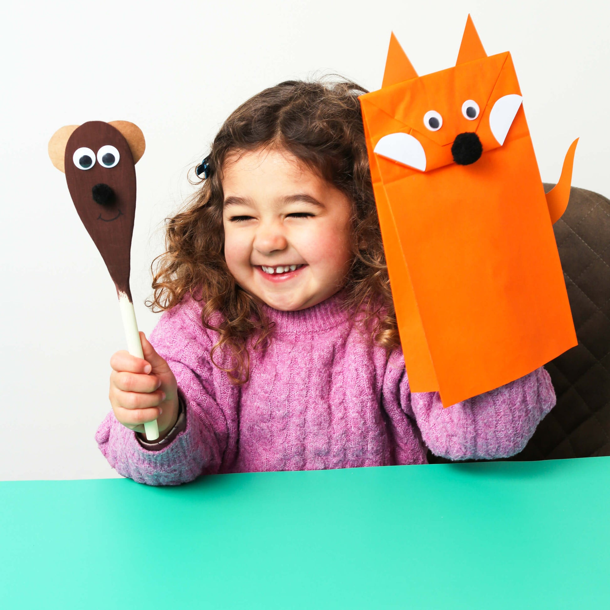 Child holding a paper mache animal and a cardboard fox mask on a white background