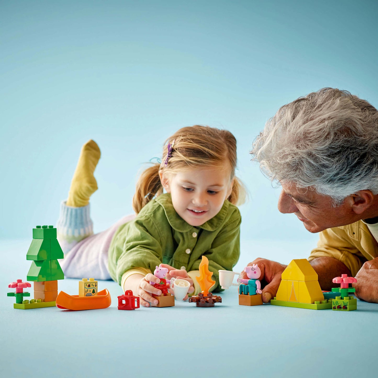 Child and elderly person playing with colorful building blocks on a light blue background