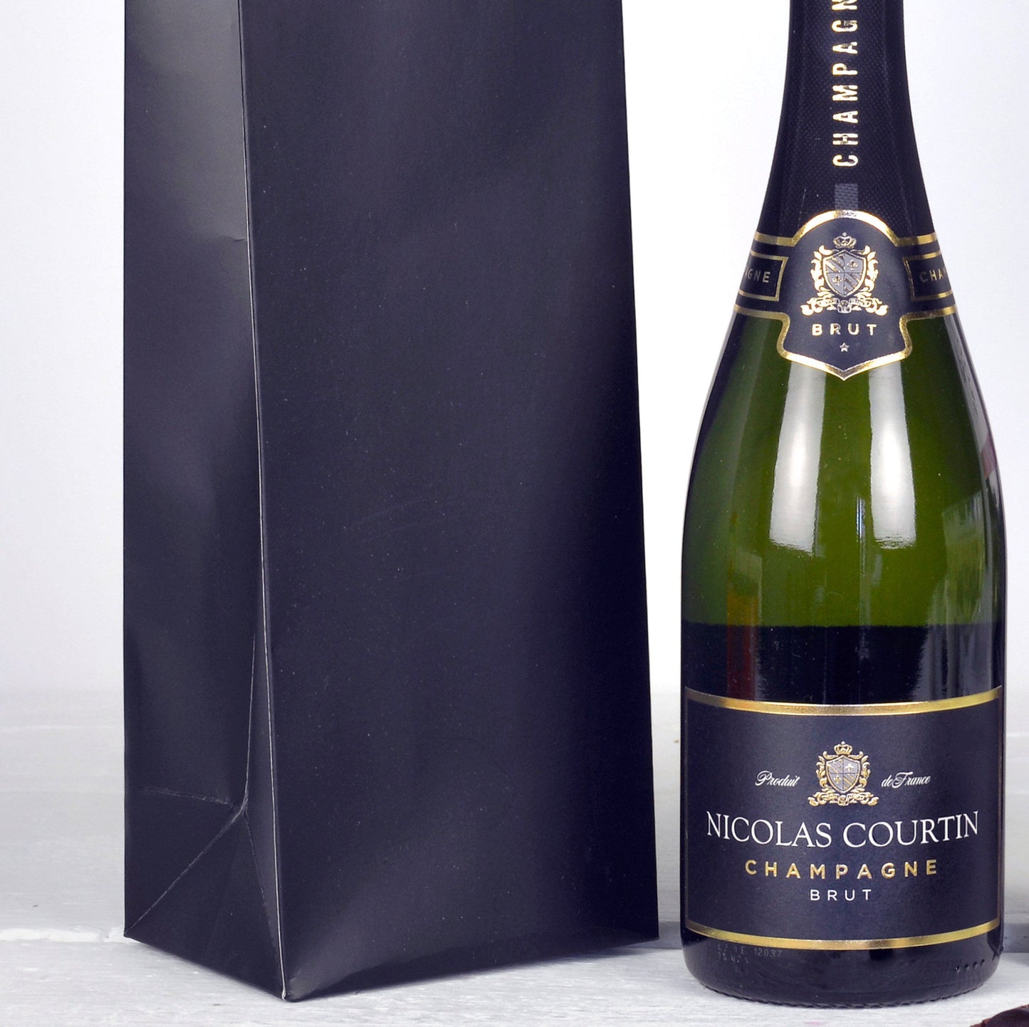 Bottle of Nicolas Courtin Champagne with a matching black gift bag on a white background