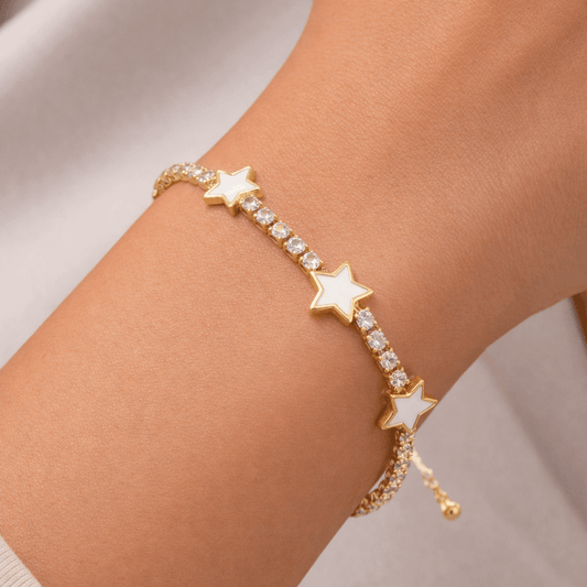 Gold bracelet with star-shaped charms on a wrist against a neutral background